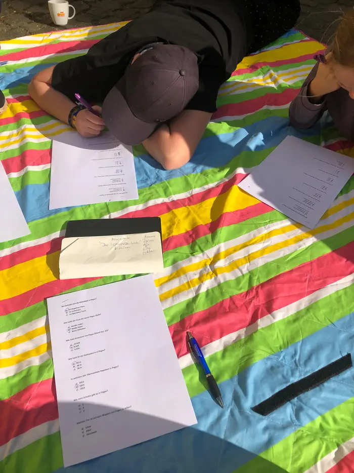 Ein Kind liegt auf einer gestreiften Decke und schreibt etwas auf ein Blatt.