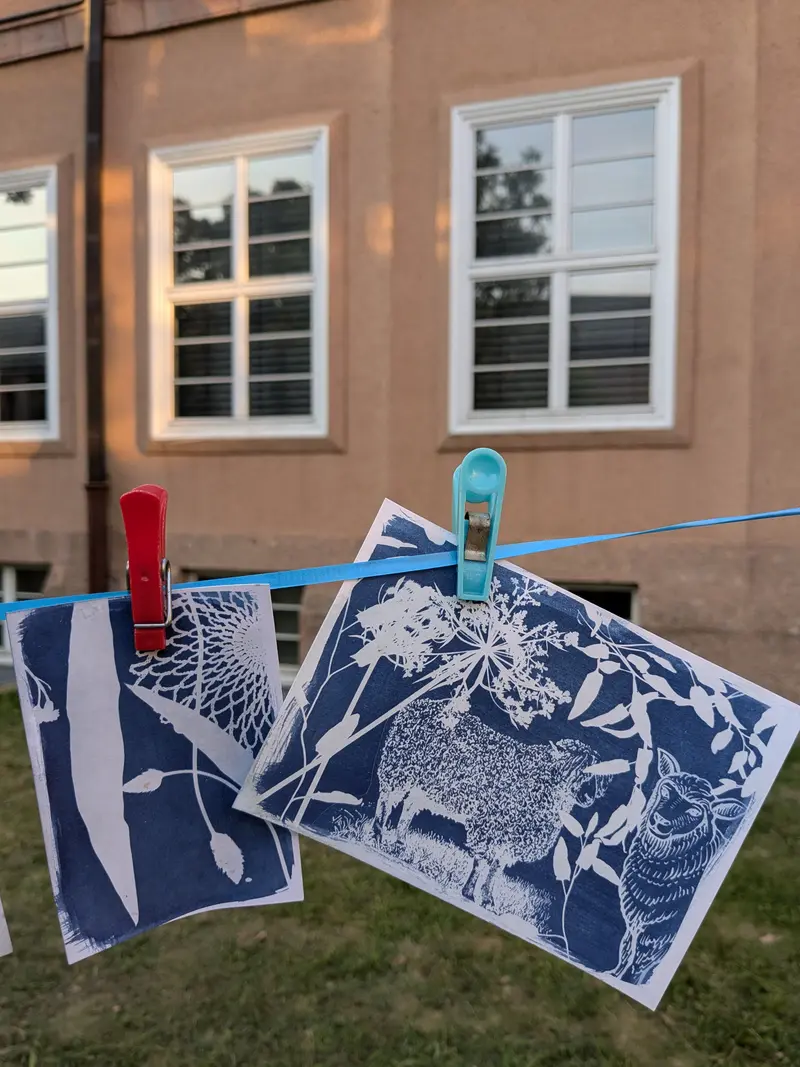 Zwei Blaudrucke hängen an einer Wäscheleine. im Hintergrund ist eine sommerliche Wiese und das Gebäude des Museums zu sehen.